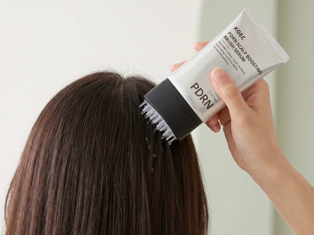 Una mano aplica el sérum en la raíz del pelo con el cepillo aplicador